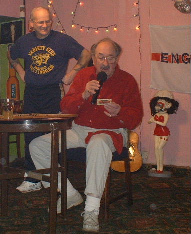 Gordon Cragg seated at bingo board reading a note on a beer mat with Oz stood behind